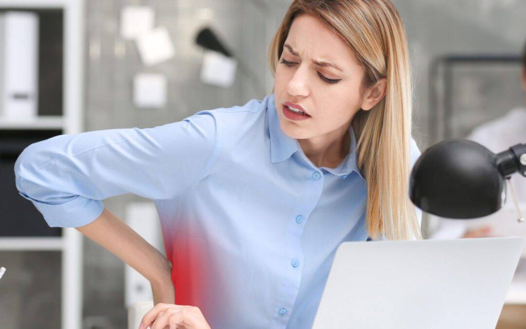 Young woman suffering from back pain at table in office