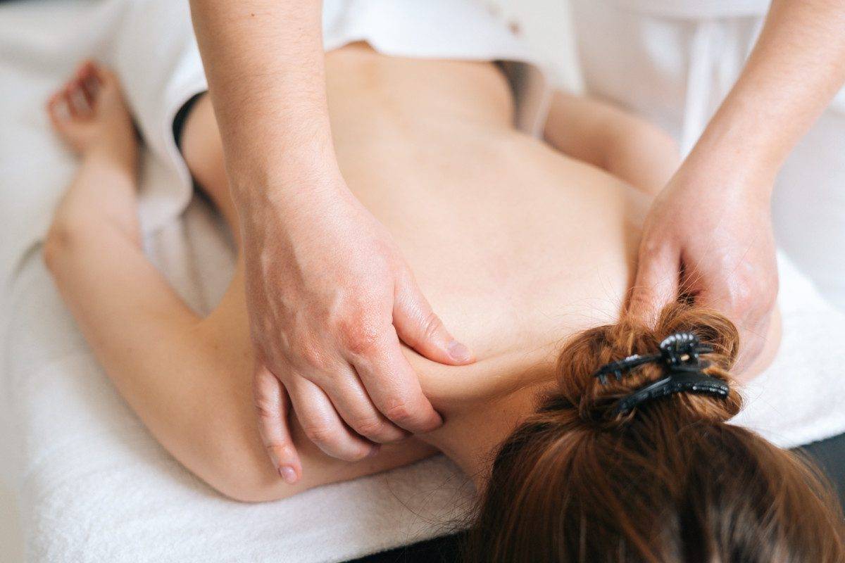 Male masseur with strong hands professionally massaging scapulas and shoulders to female client.