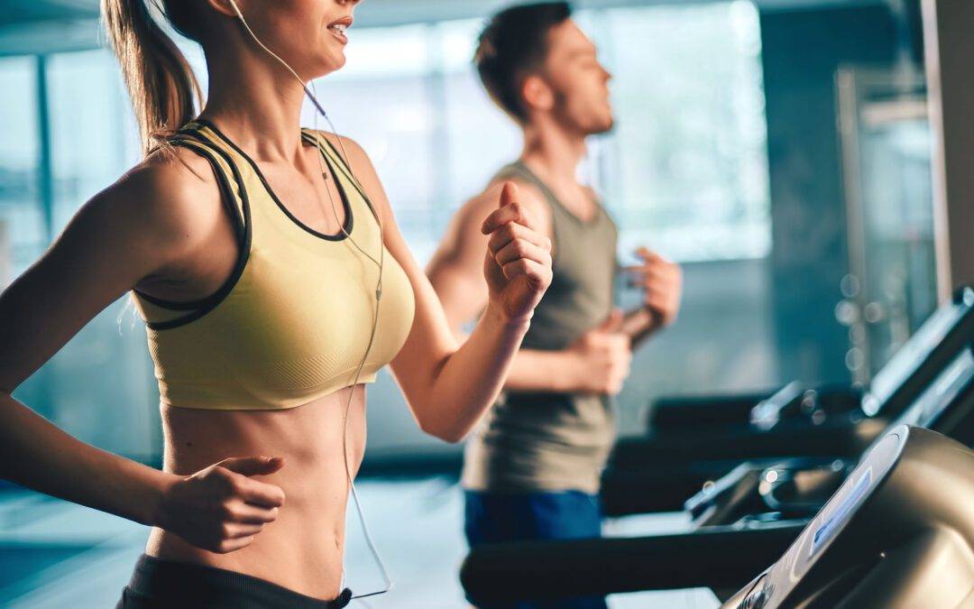 Girl with earphones running on treadmill and listening to music with guy on background